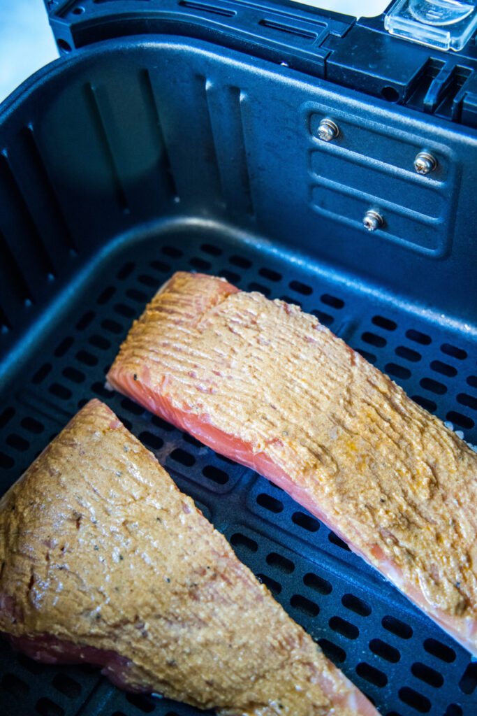 Two uncooked salmon fillets covered with a mustard rub in an air fryer basket.