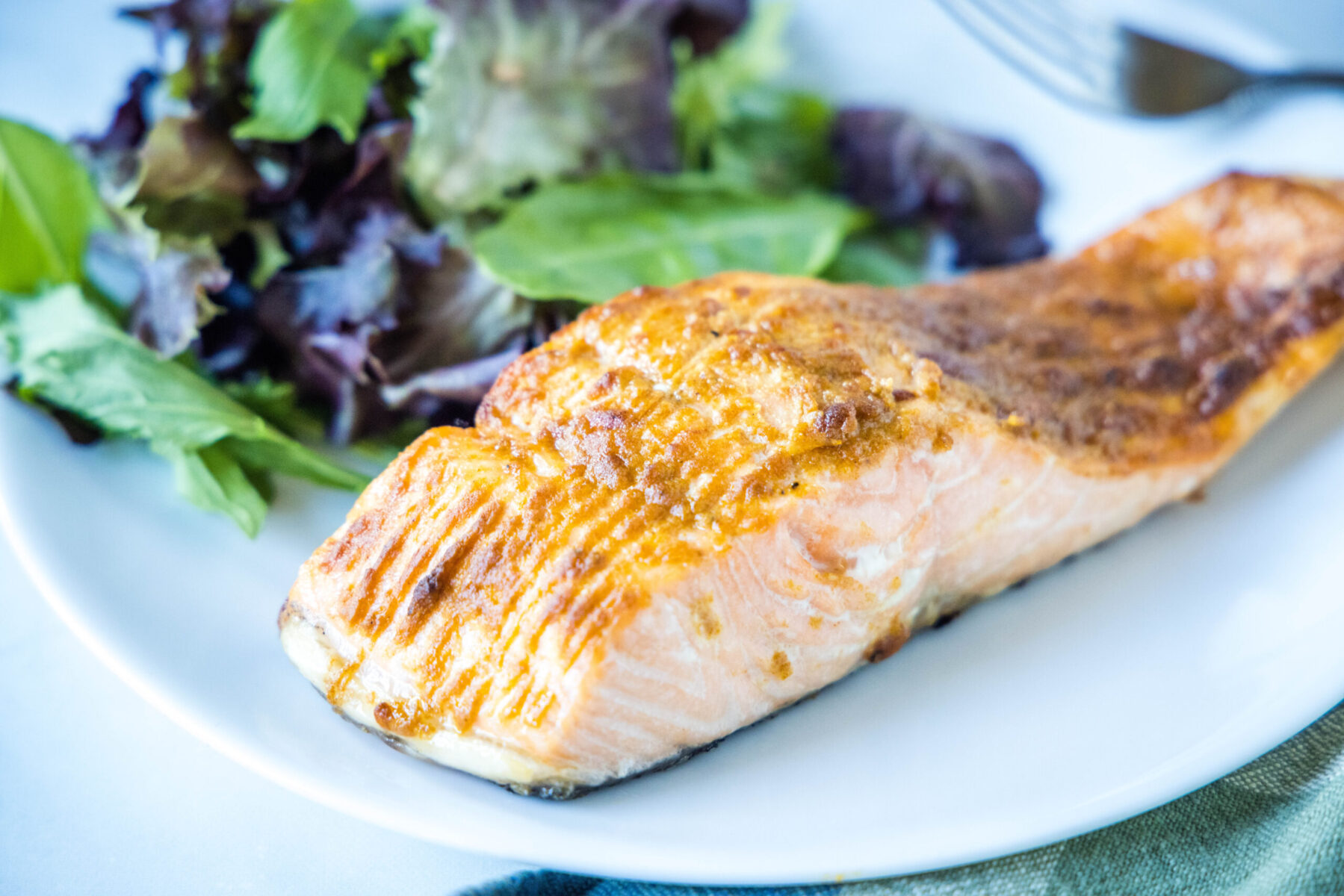 A salmon fillet on a plate with a salad.