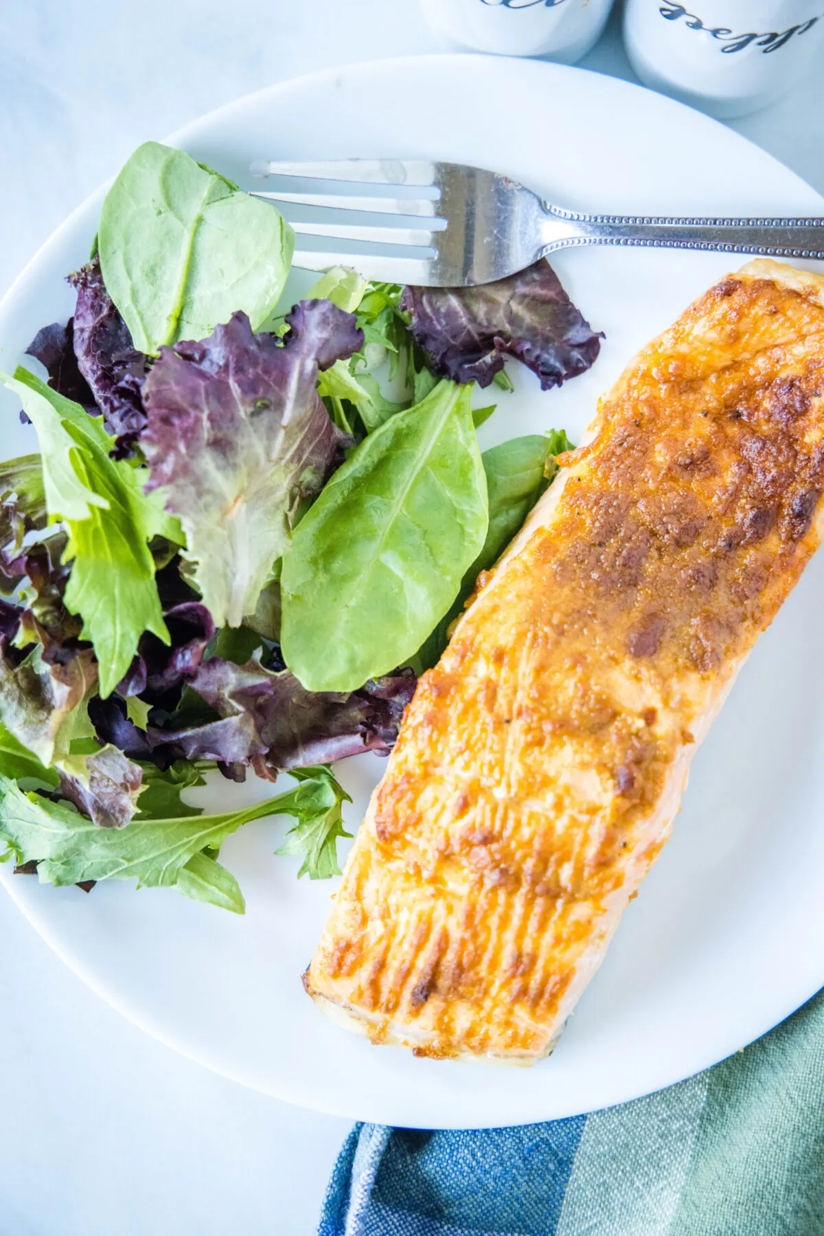 Overhead view of a plate with a salmon fillet, a green salad, and a fork.