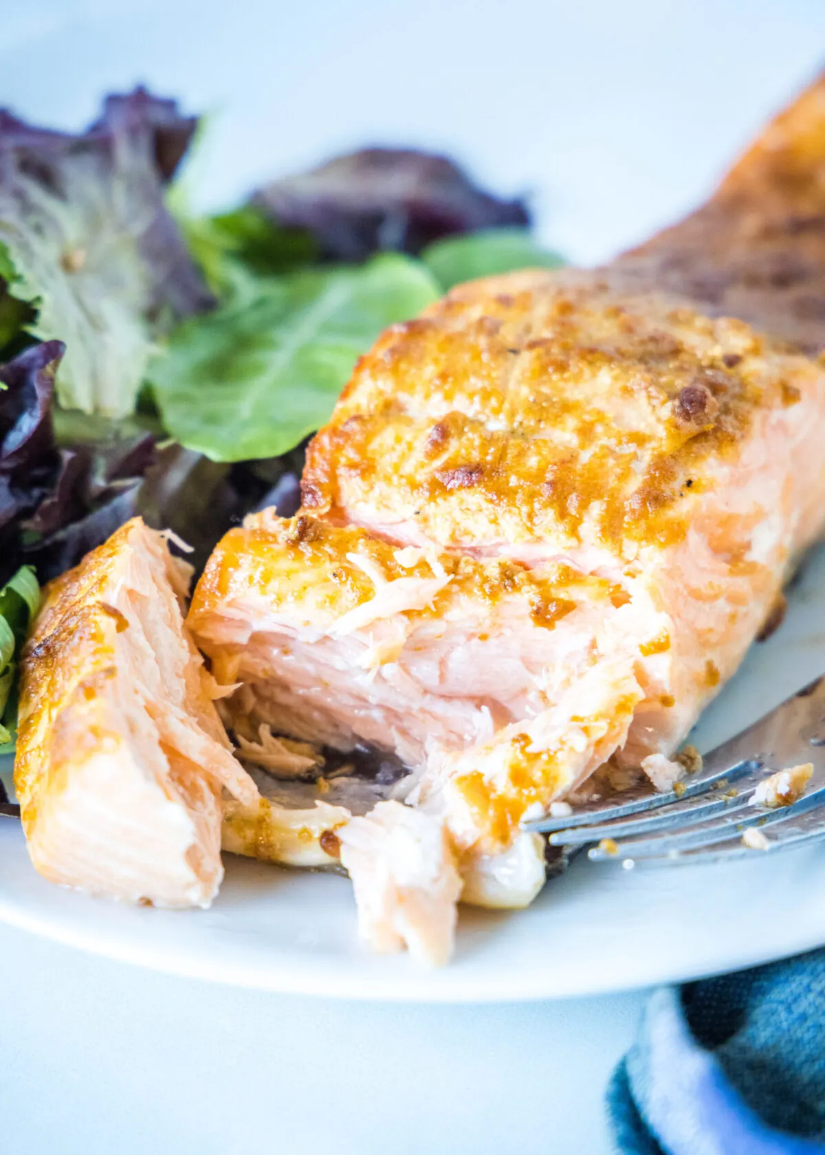Close up of a fork cutting through a salmon fillet on a plate with a salad.