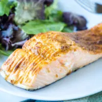 Close up of a salmon fillet on a plate with a salad.