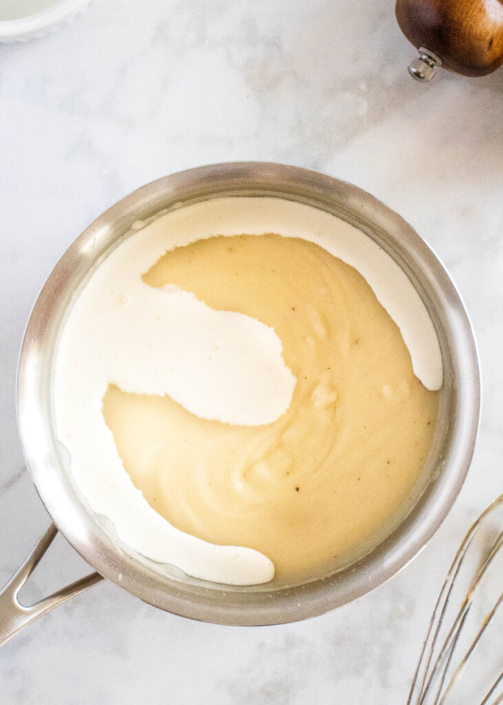 Overhead view of a saucepan with a thickened roux, with heavy cream on top.