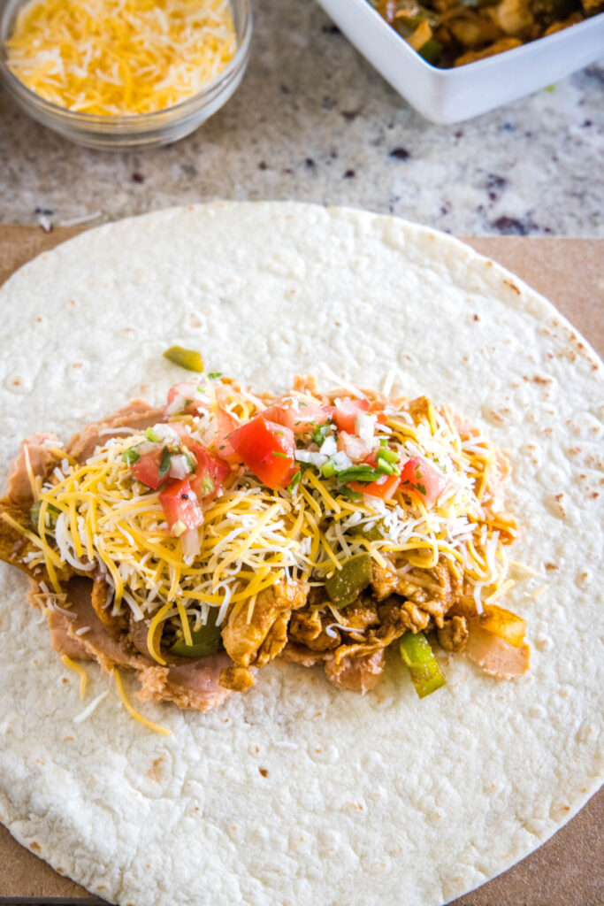 A tortilla topped with beans, chicken and veggies, cheese, and pico de gallo.