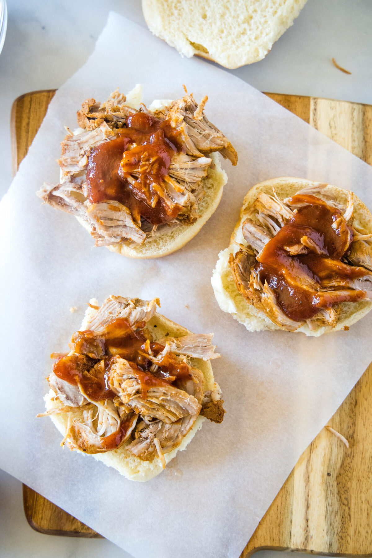 Overhead view of three bottom slider buns topped with pulled pork and barbecue sauce.