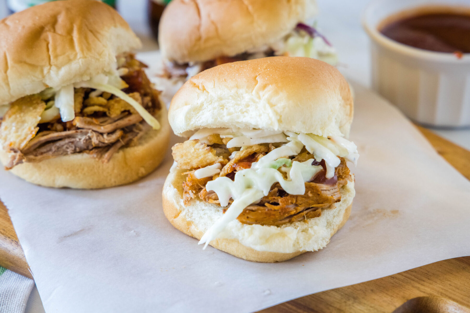 Three pulled pork sliders next to a bowl of barbecue sauce.