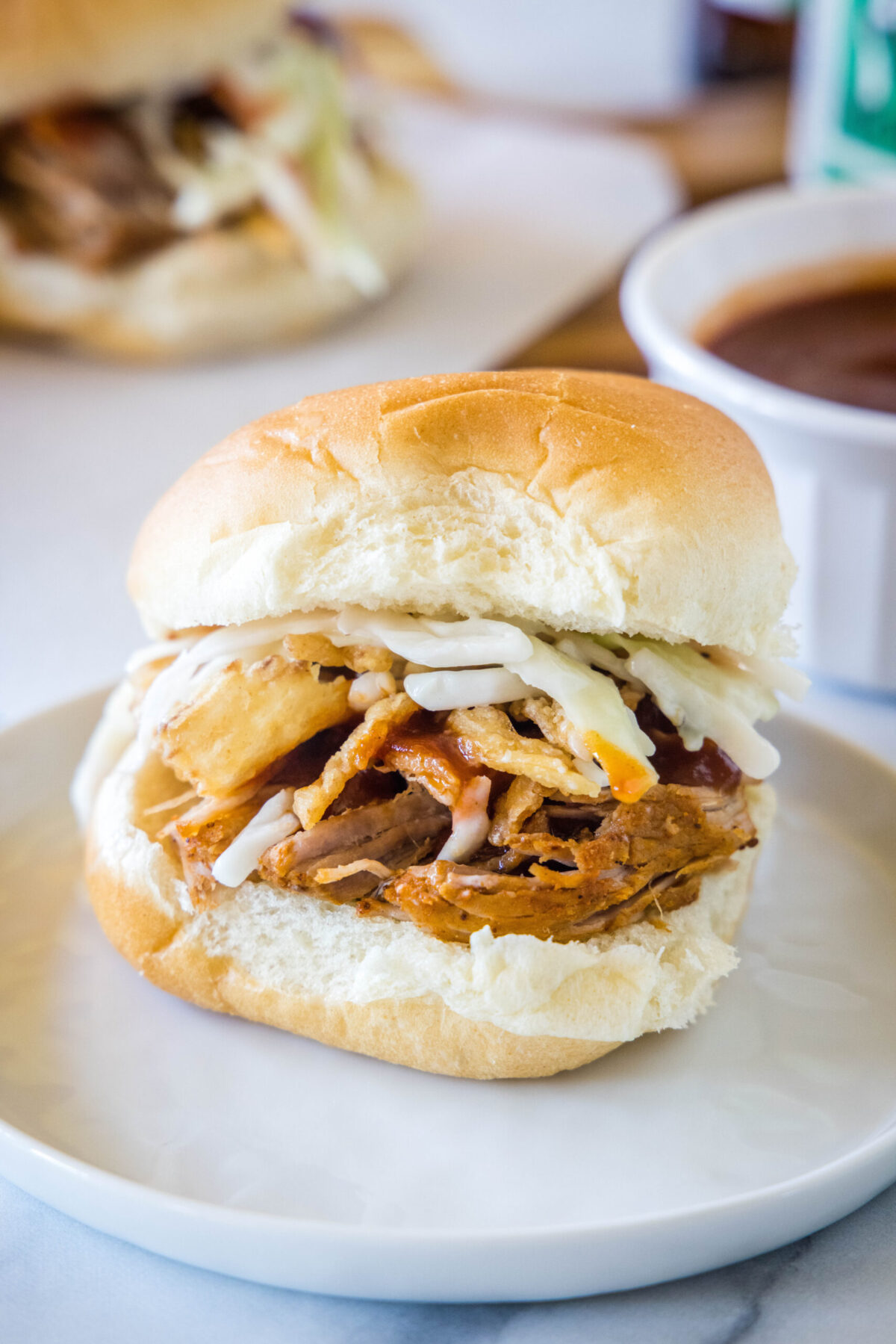 A pulled pork slider with coleslaw on a plate, with another one in the background.