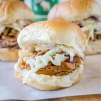 Close up of a pulled pork slider with coleslaw, with two more in the background.