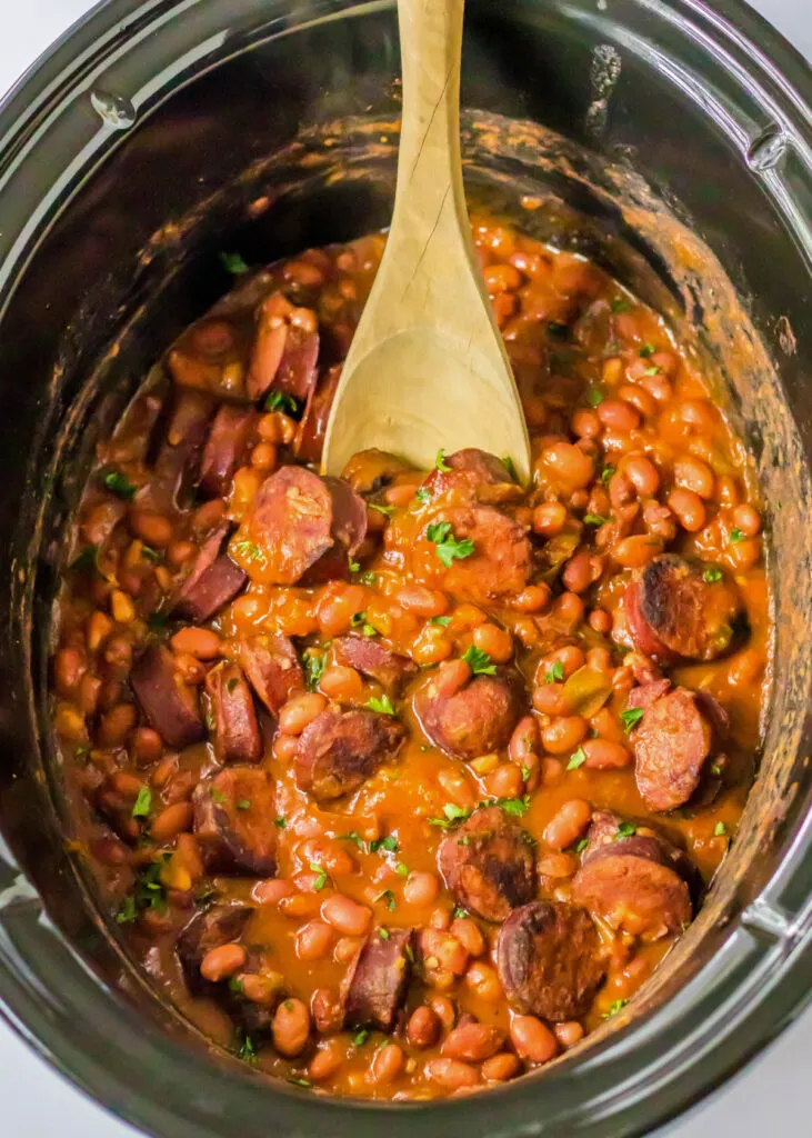 Overhead view of cooked red beans and rice in a slow cooker with a wooden spoon.