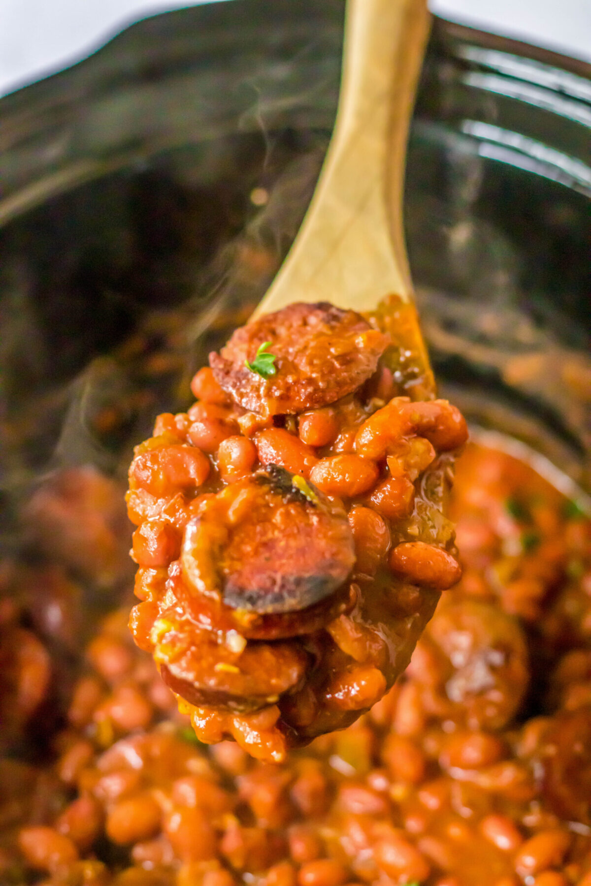 Red beans and sausage cooking in a crockpot, with a wooden spoon removing a spoonful.