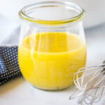 A jar of apple cider vinaigrette on a countertop next to a whisk.