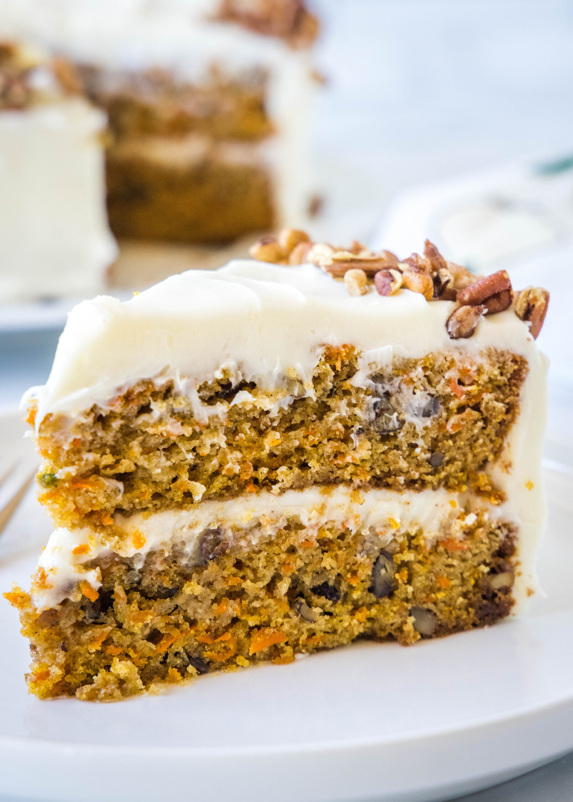 A slice of frosted carrot cake on a white plate.