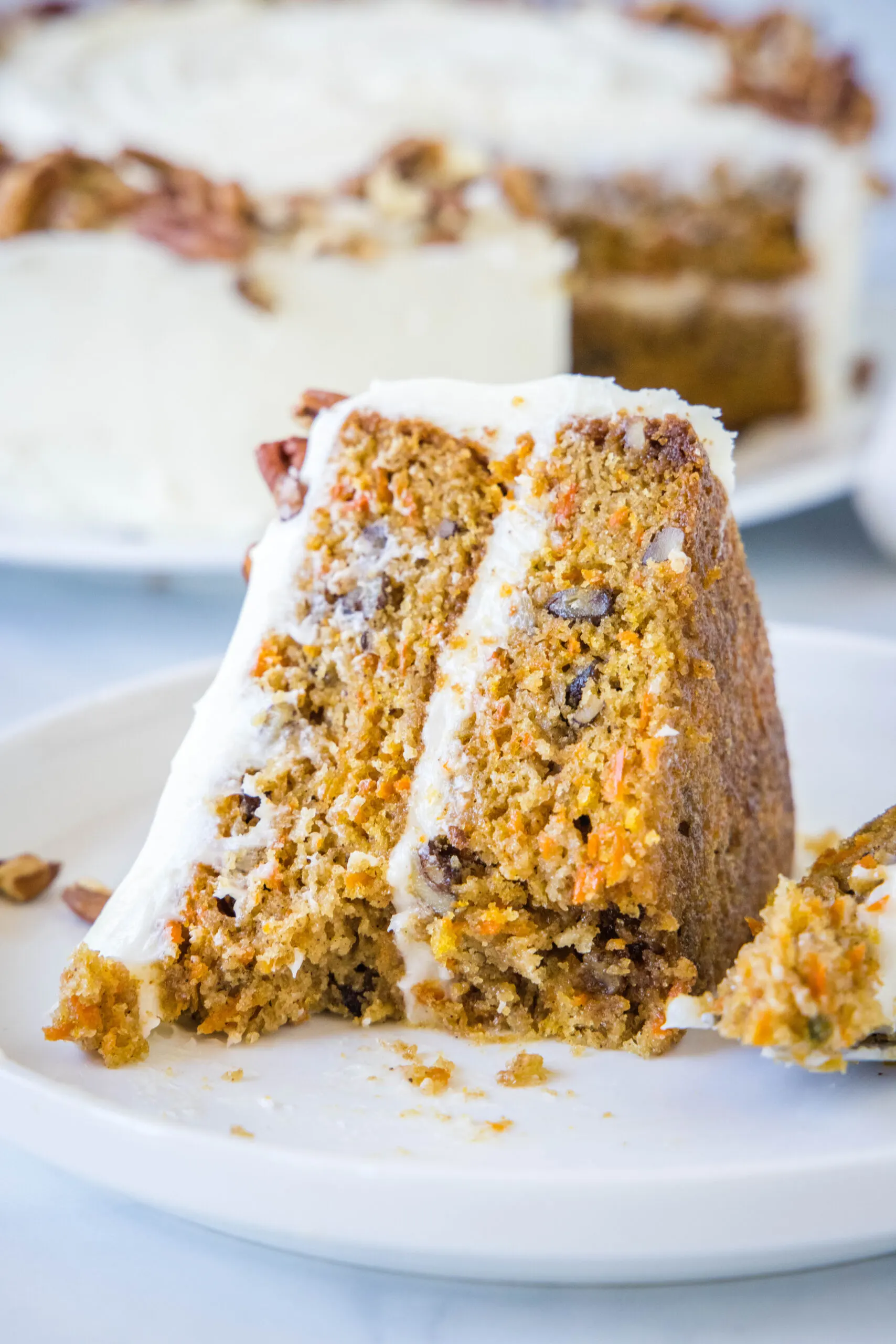 A slice of frosted carrot cake on a white plate with forkfuls missing.