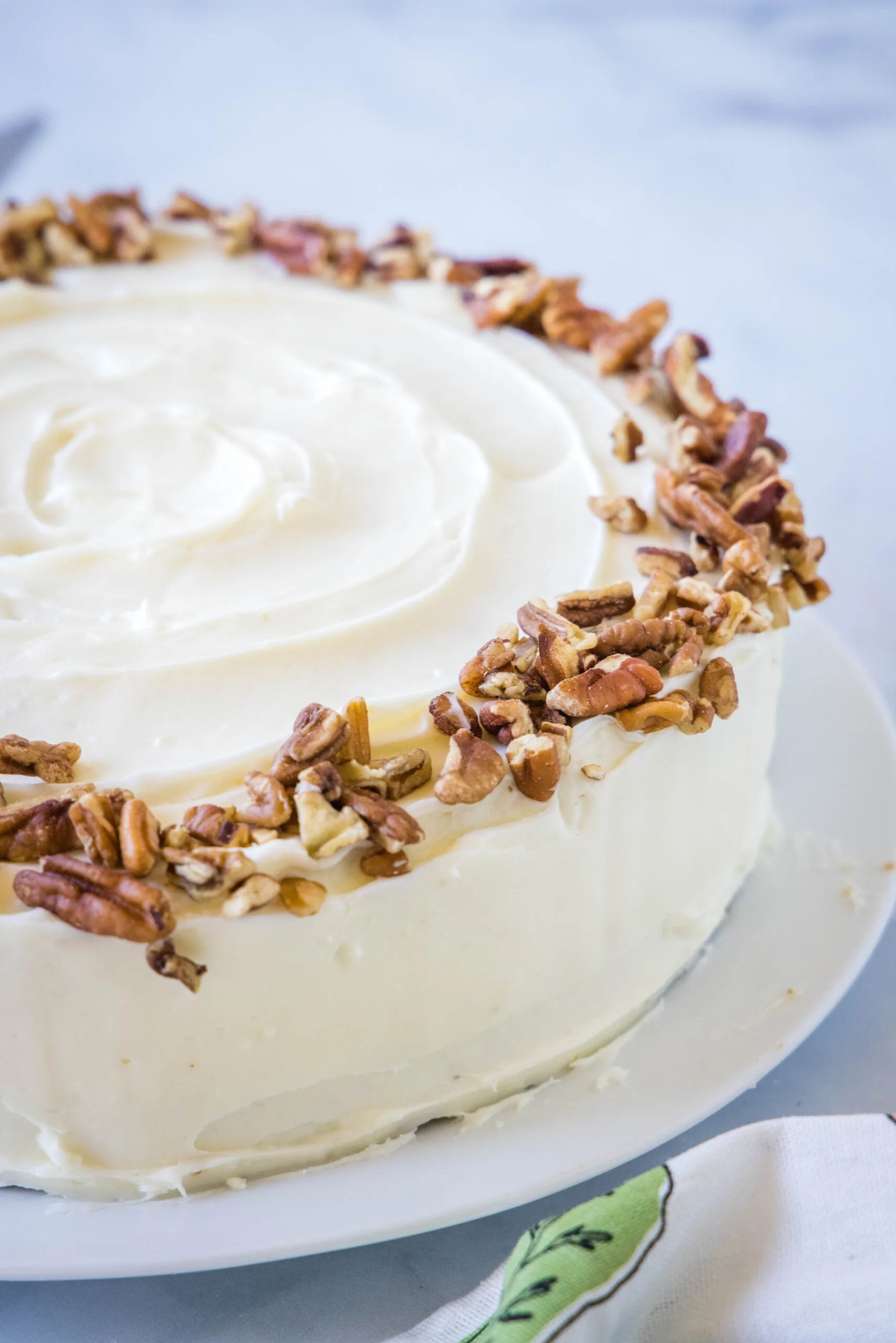A whole carrot cake frosted with cream cheese frosting and garnished with chopped pecans.
