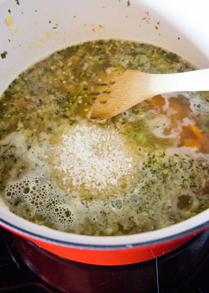 Rice added to a pot of chicken soup stock, with a wooden spatula for stirring.