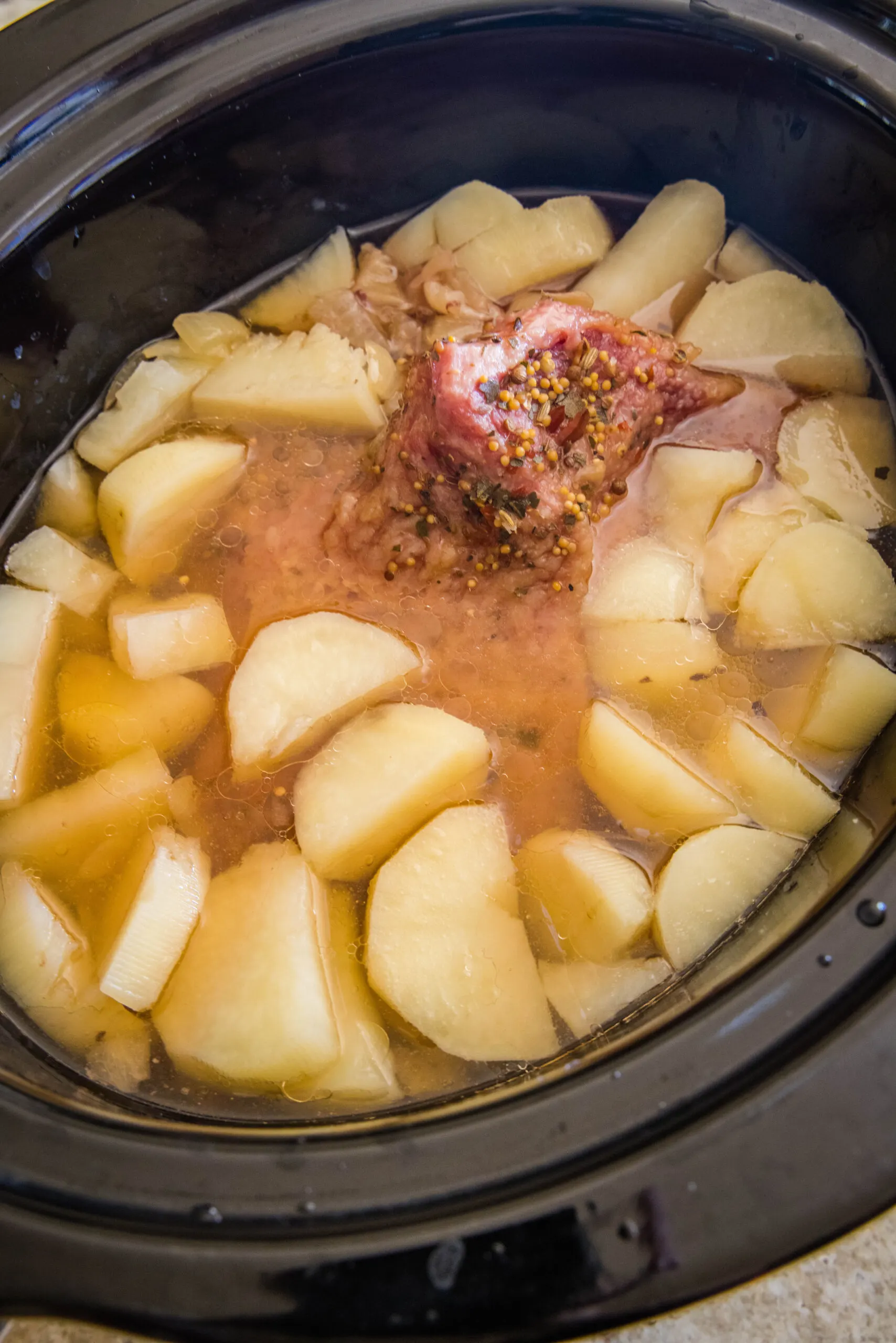 Cooked corned beef, onions, and potatoes inside the slow cooker.