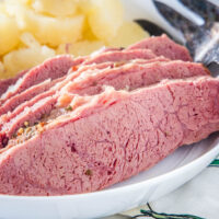Sliced corned beef on a white plate with cooked onions in the background.