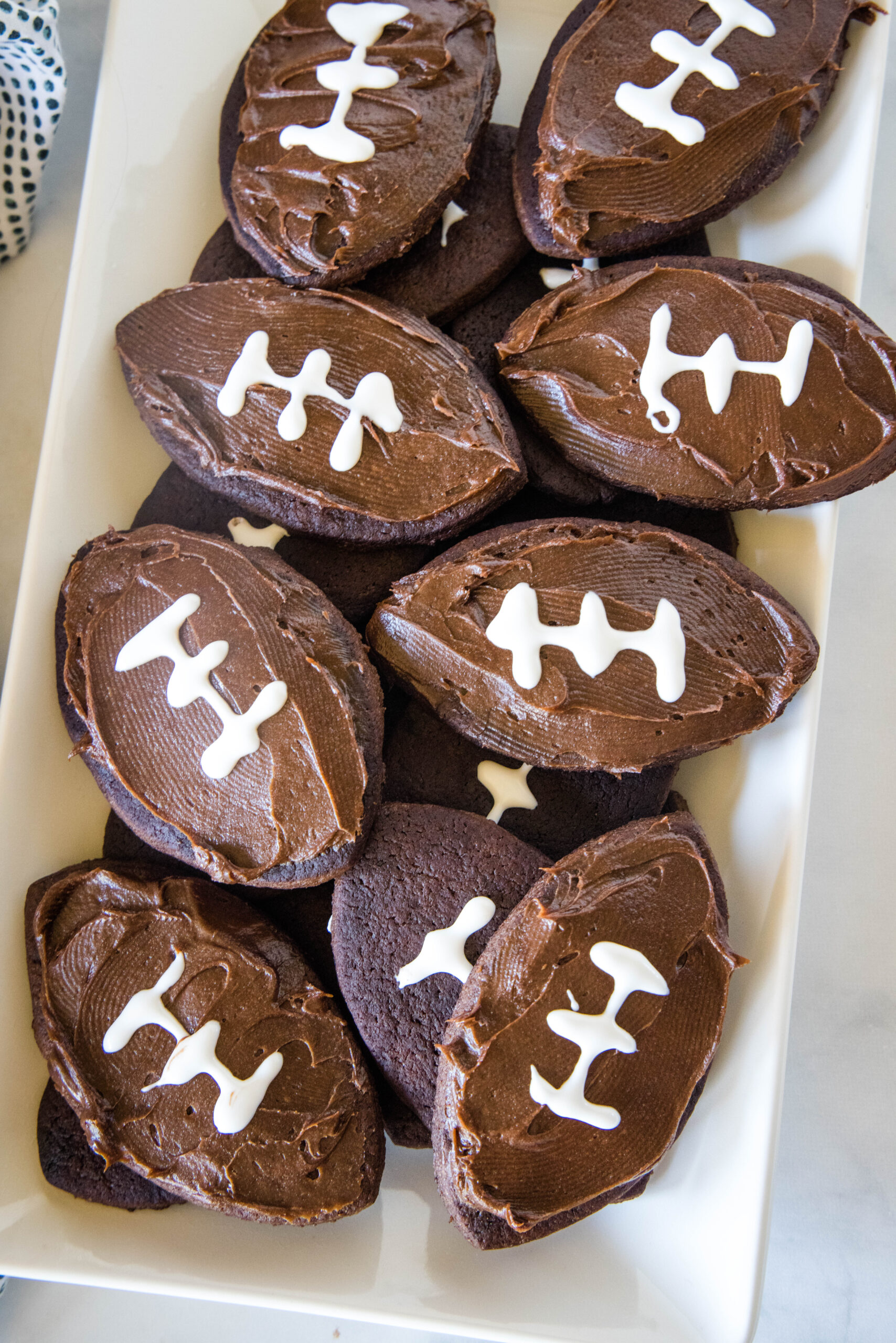 Overhead view of assorted frosted football cookies on a rectangular white plate.