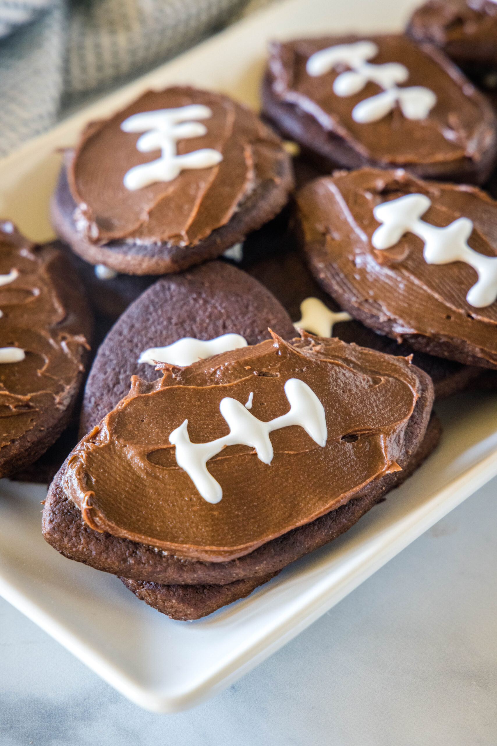 Assorted frosted football cookies on a rectangular white plate.
