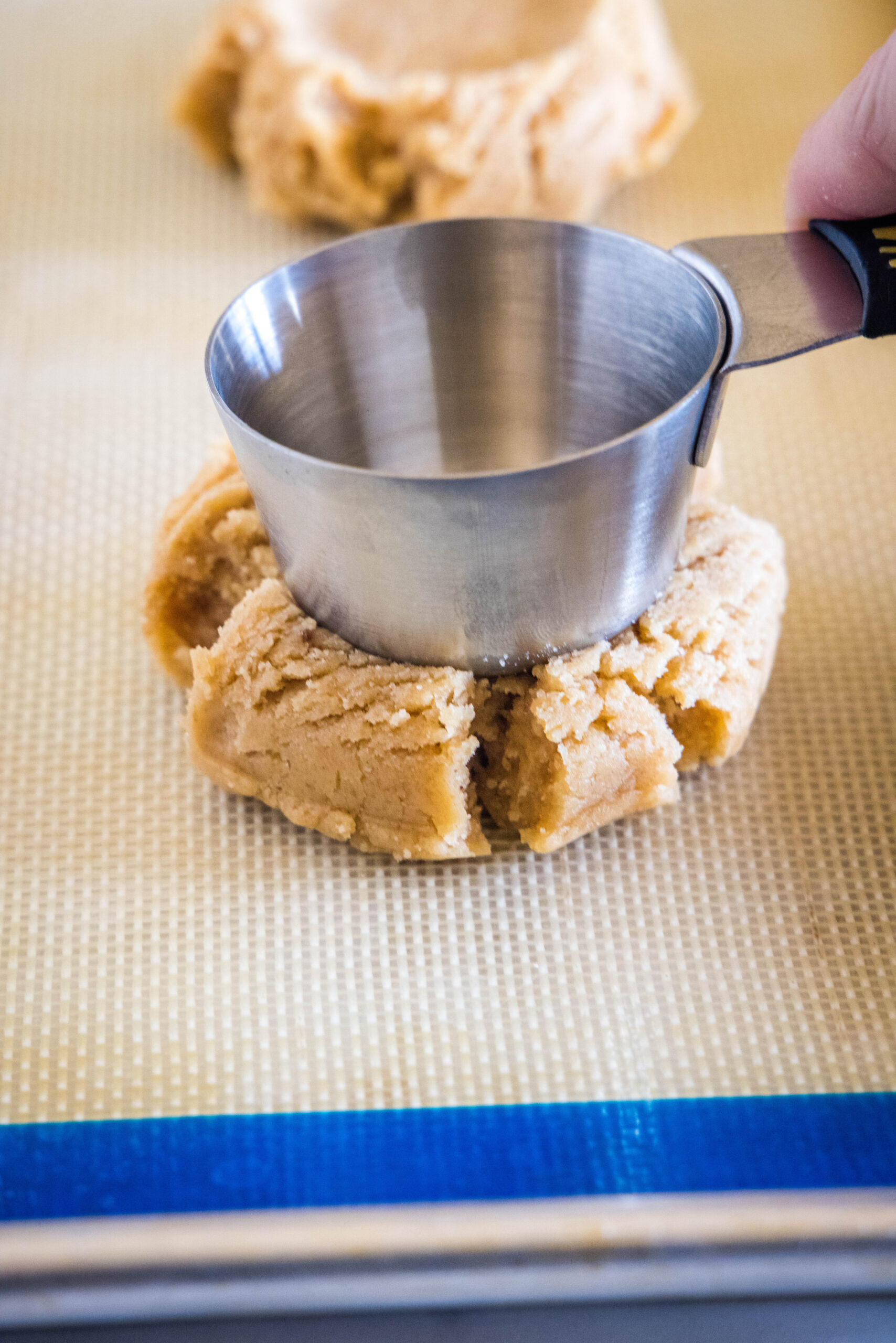 using a measuring cup to press down cookie dough