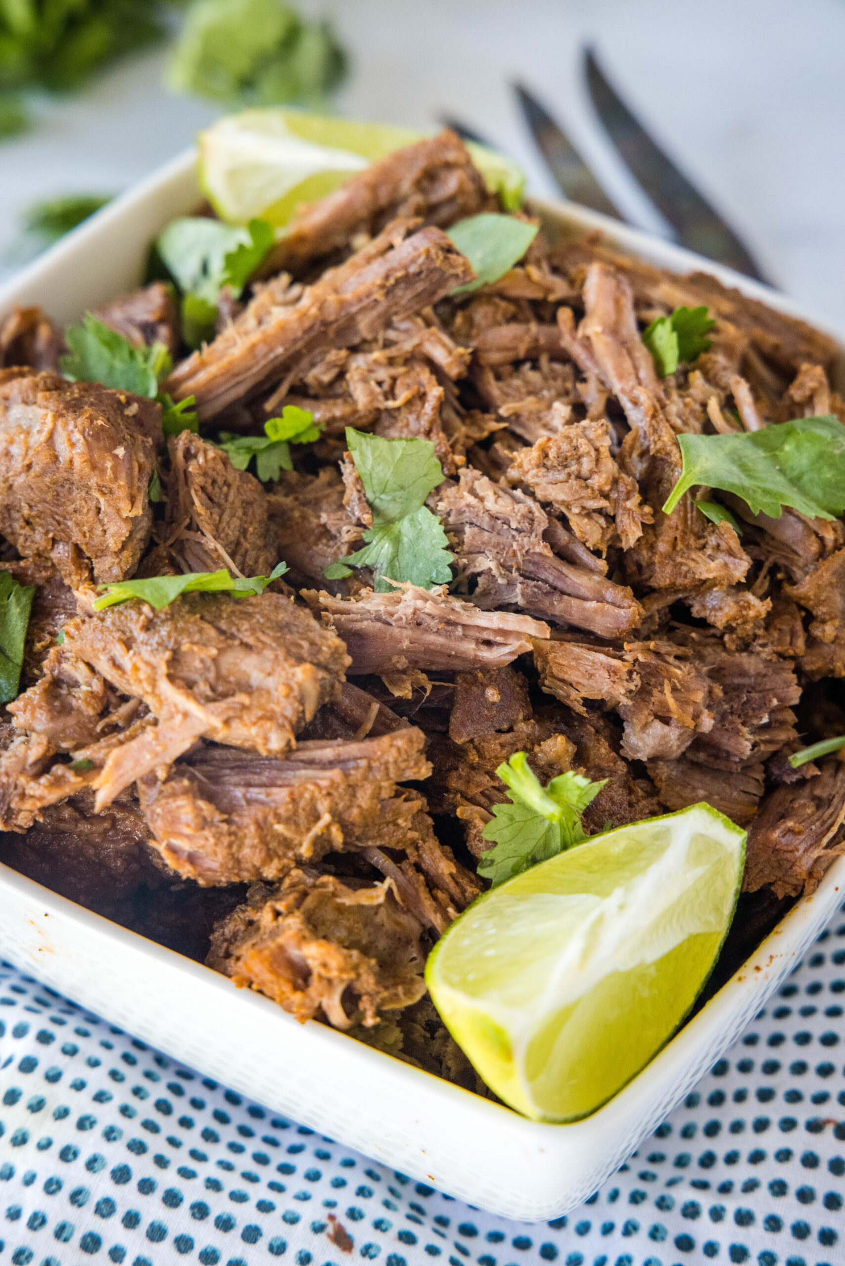 Mexican shredded beef in a square bowl garnished with cilantro and a lime wedge.