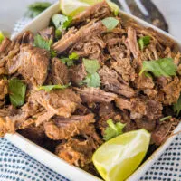 Mexican shredded beef in a square bowl garnished with cilantro and a lime wedge.