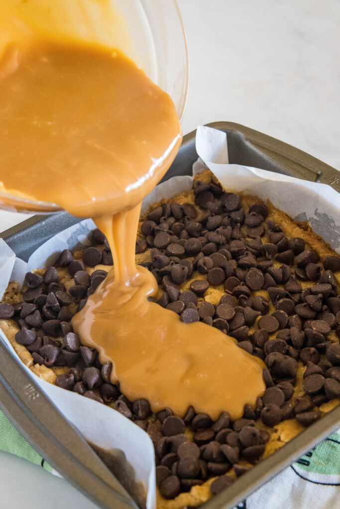 pouring melted caramel over chocolate chips in a baking dish