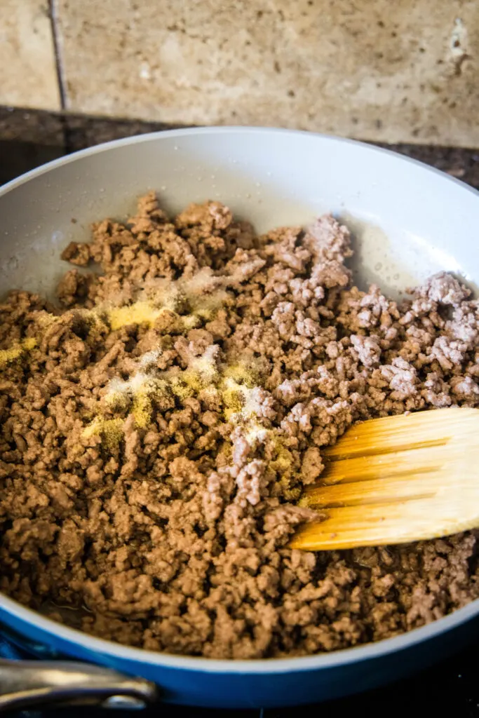 A wooden spatula stirring ground beef as it cooks in a skillet.