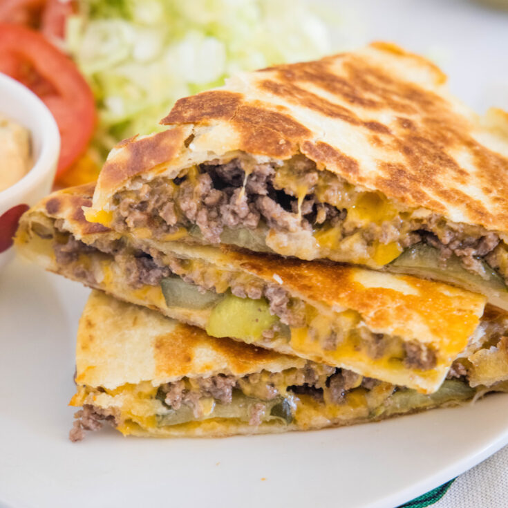 Three slices of cheeseburger quesadilla stacked on a plate.