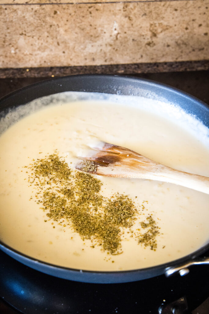 Seasoning added to cream sauce in a skillet, with a wooden spoon.