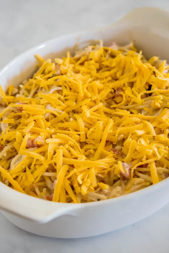 Chicken spaghetti covered with shredded cheese in an oval casserole dish.