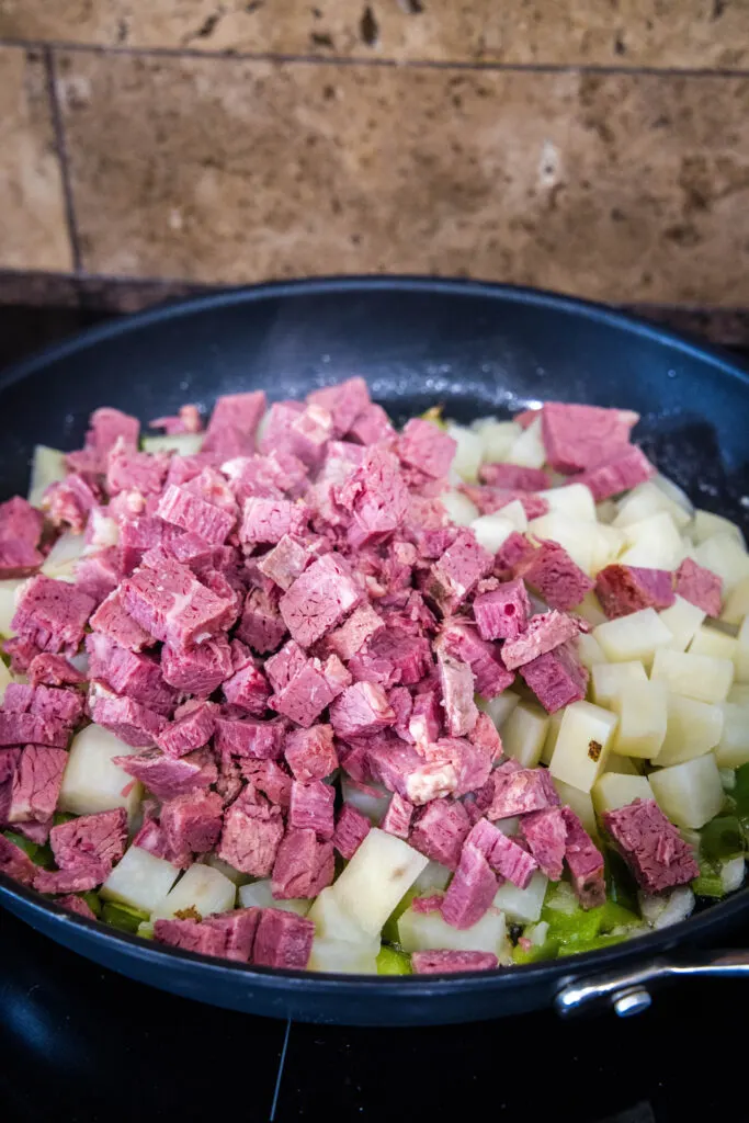 Chopped corned beef added to a skillet with diced sauteed onions and peppers.