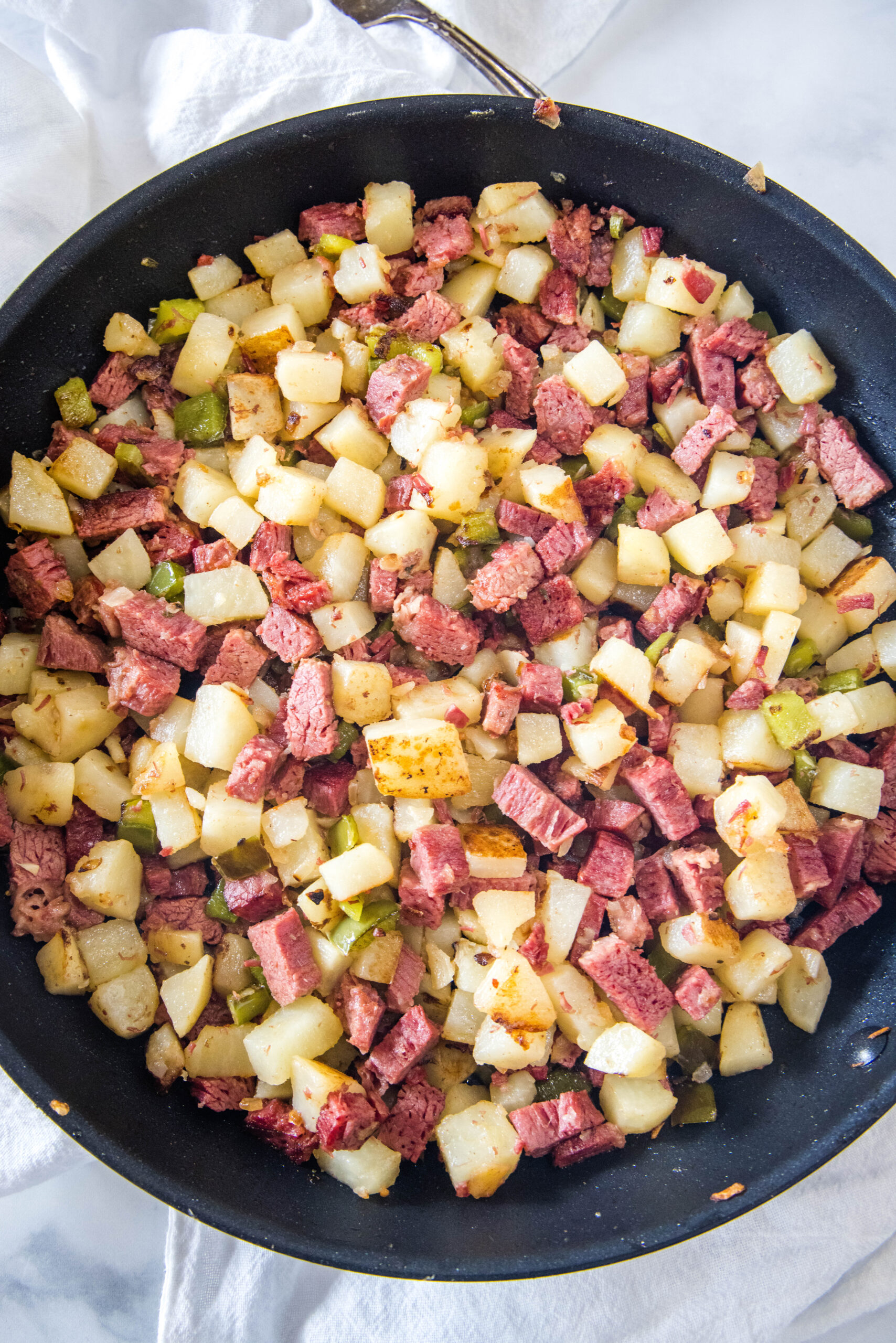 Overhead view of diced potatoes, chopped corned beef, onions, and bell peppers combined in a skillet for corned beef hash.