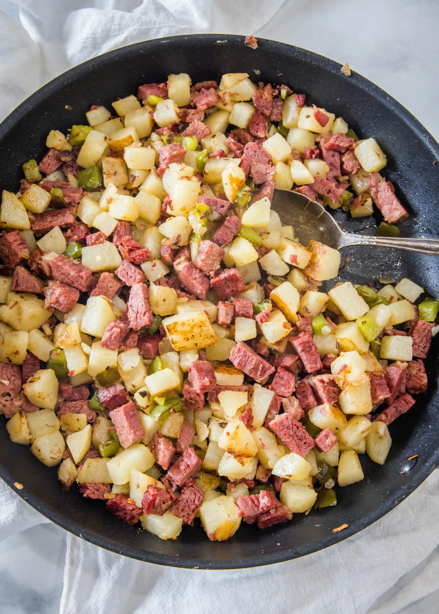 Overhead view of corned beef hash in a large skillet with a serving spoon.