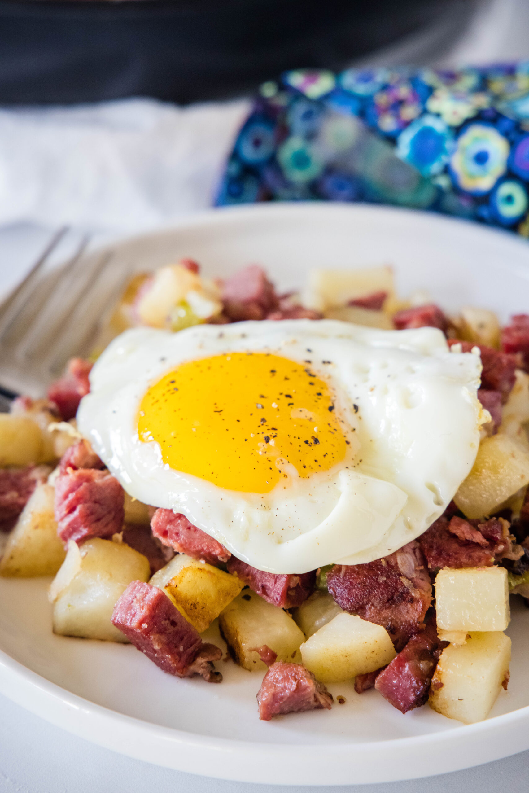 Fried egg served over a bed of corned beef hash on a white plate.