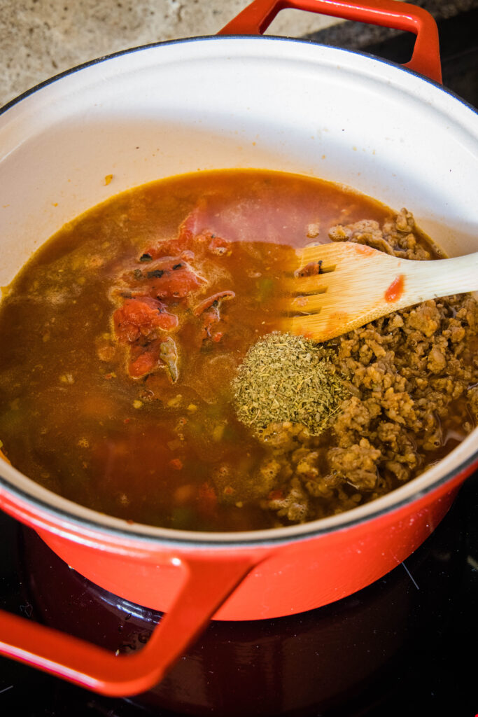 Italian sausage soup simmering in a large pot with a wooden stirring spoon.