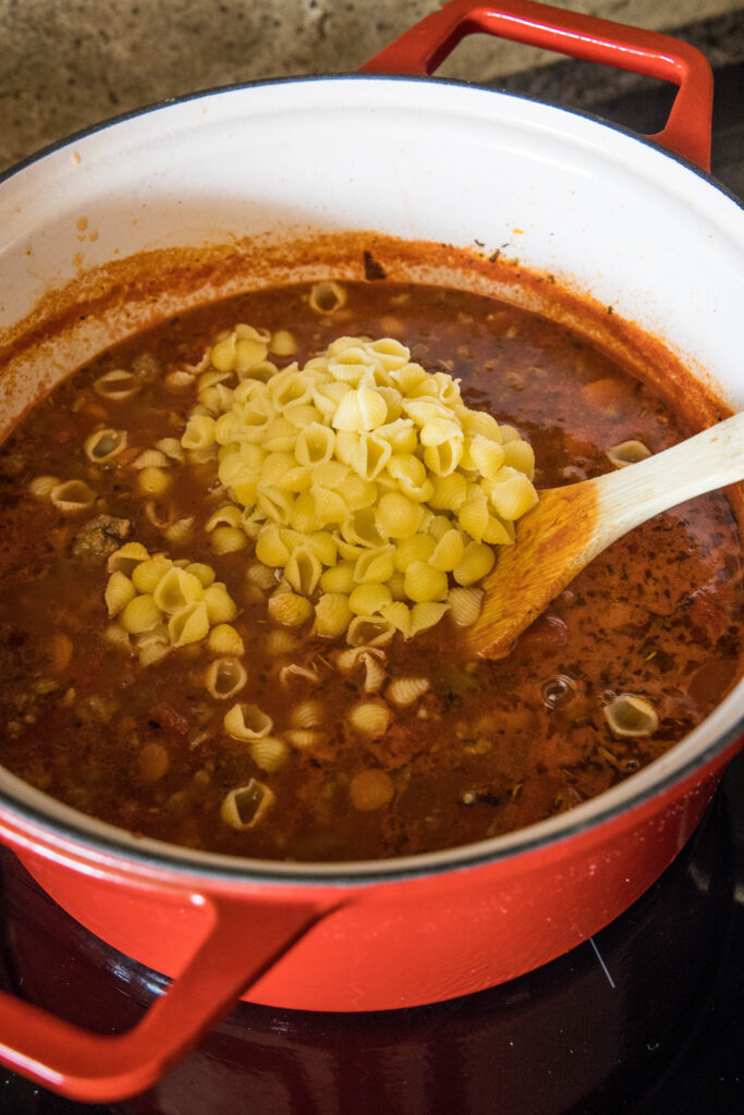 Cooked pasta noodles added to a large pot of Italian sausage soup.