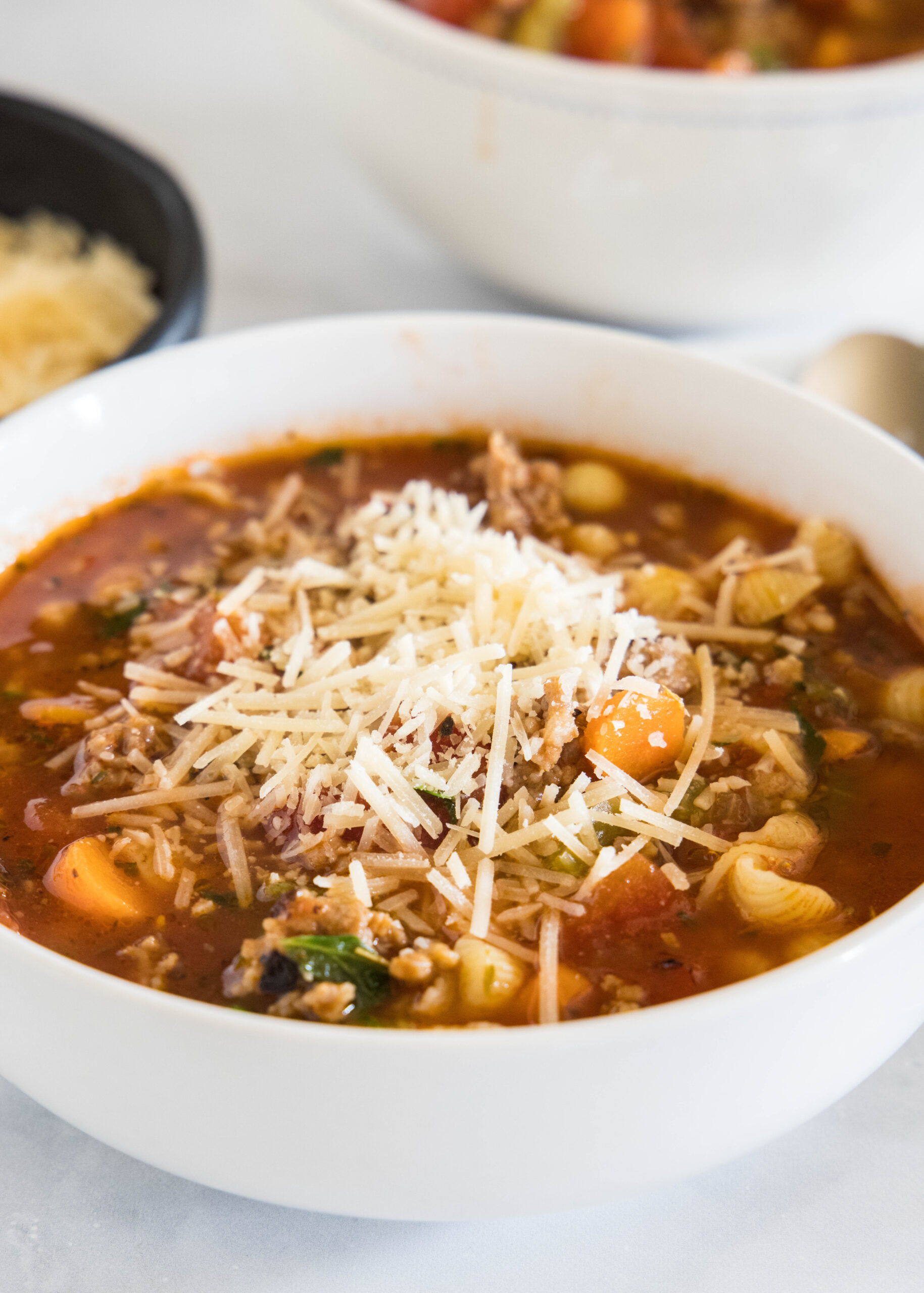A bowl of Italian sausage soup topped with shredded cheese.