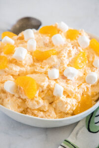 Orange fluff salad topped with mini marshmallows in a white bowl.