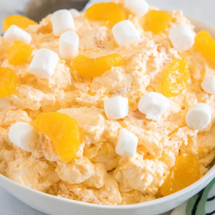 Orange fluff salad topped with mini marshmallows in a white bowl.