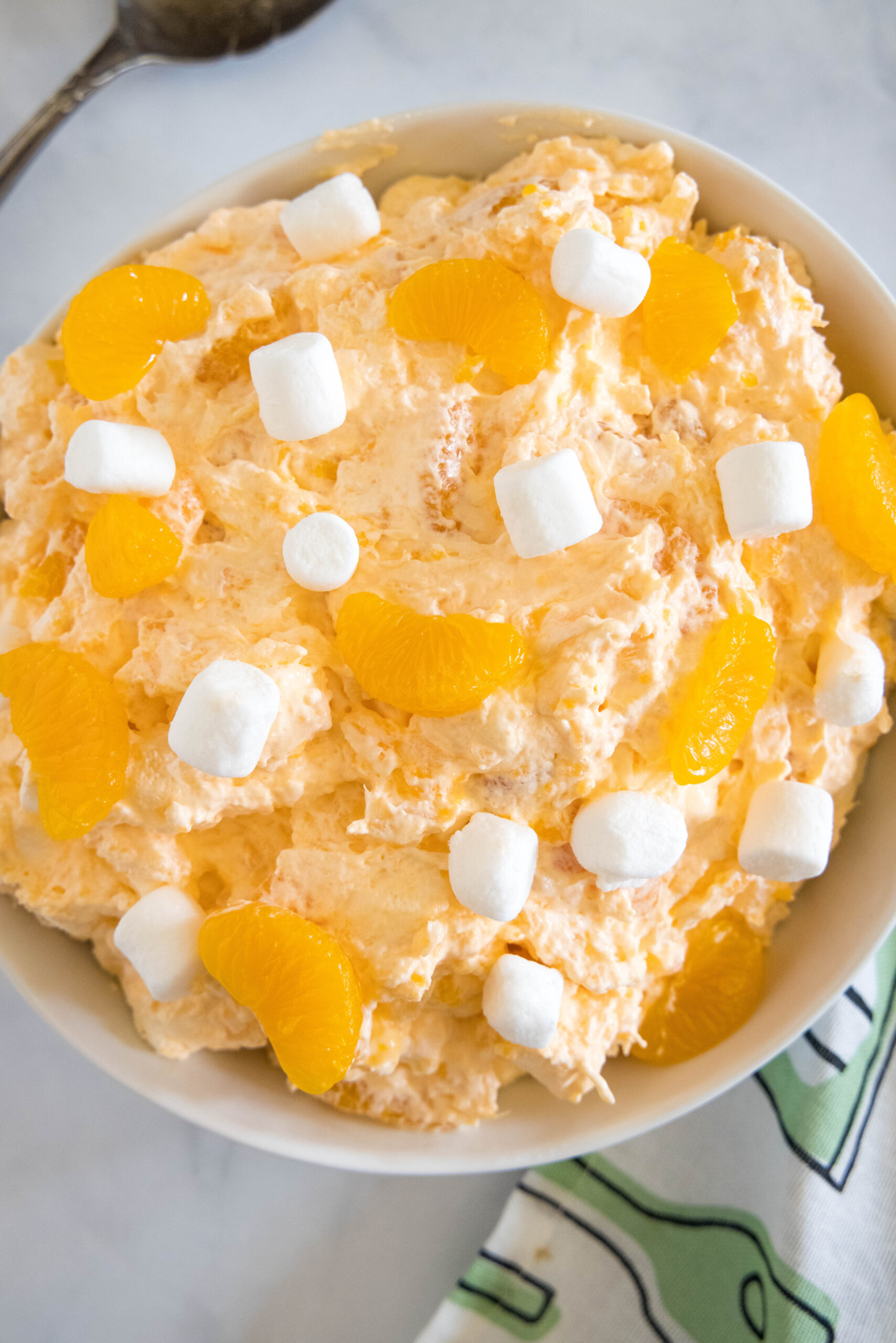 Overhead view of orange fluff salad topped with mini marshmallows in a white bowl.
