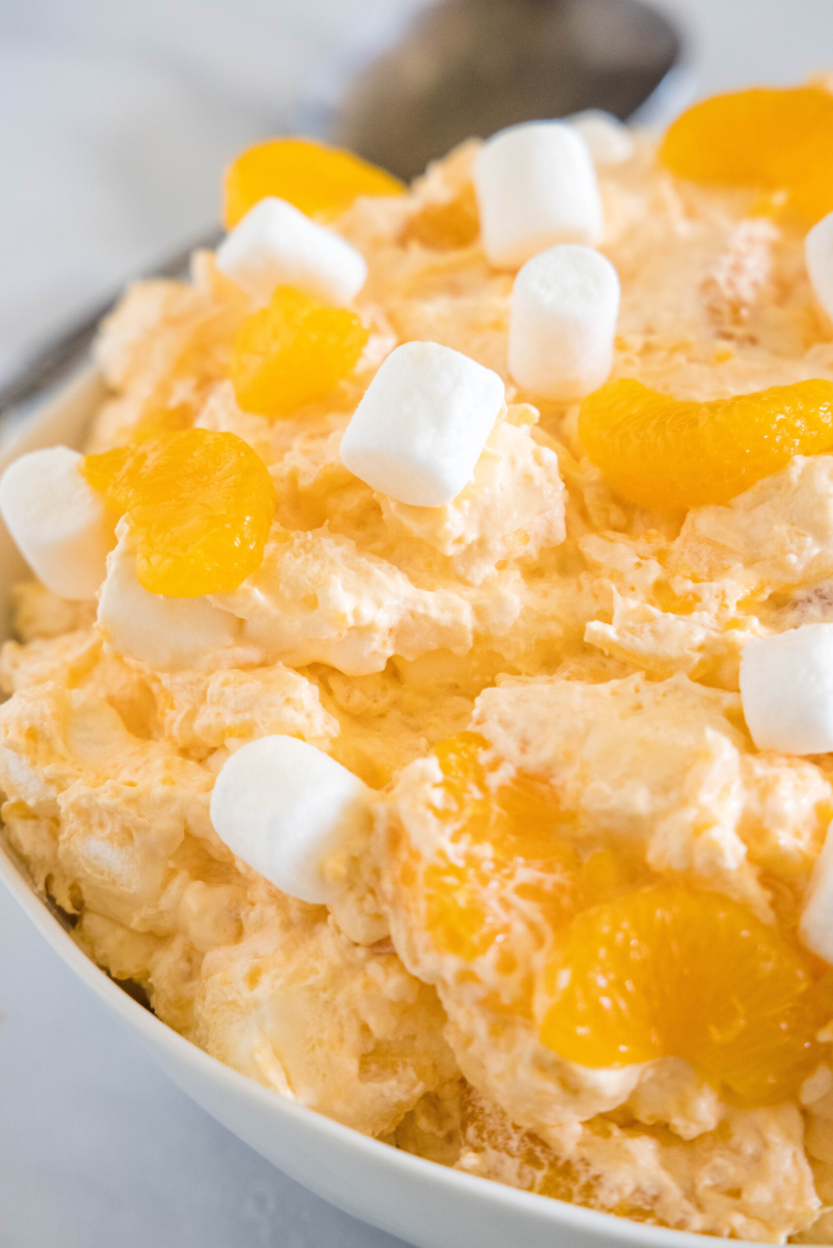 Close up of orange fluff salad topped with mini marshmallows in a white bowl.