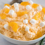 Orange fluff salad topped with mini marshmallows in a white bowl.