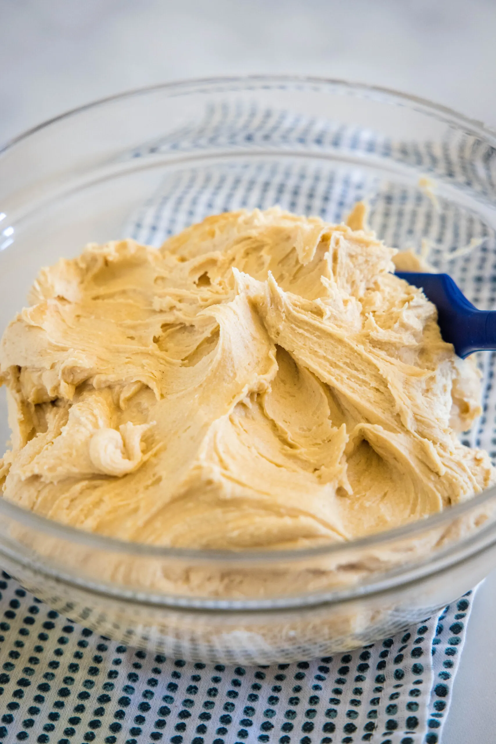Peanut butter frosting in a glass bowl with a blue stirring spoon.