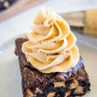 A chocolate brownie topped with a swirl of peanut butter frosting on a plate.