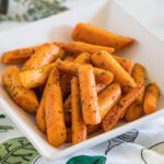 Seasoned roasted carrots in a square white bowl.