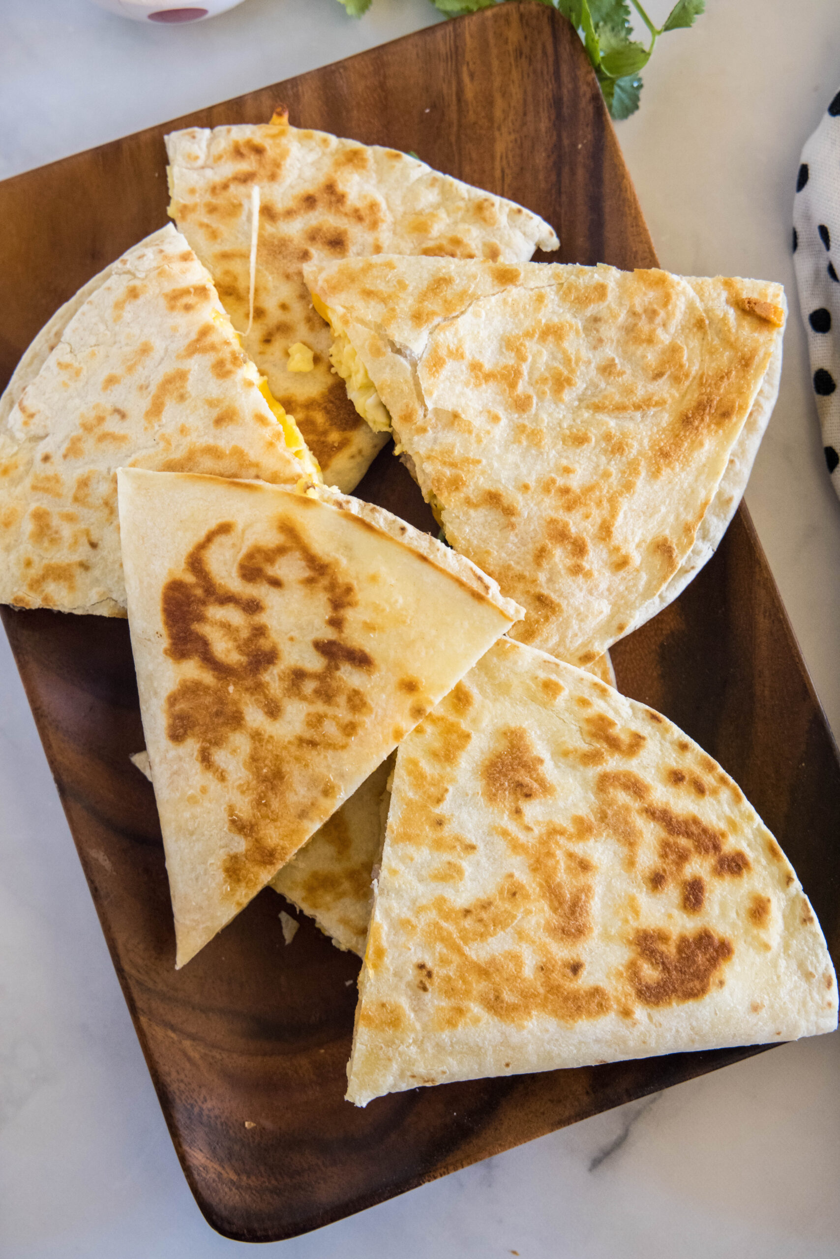 Overhead view of breakfast quesadillas stacked on a wooden serving platter.