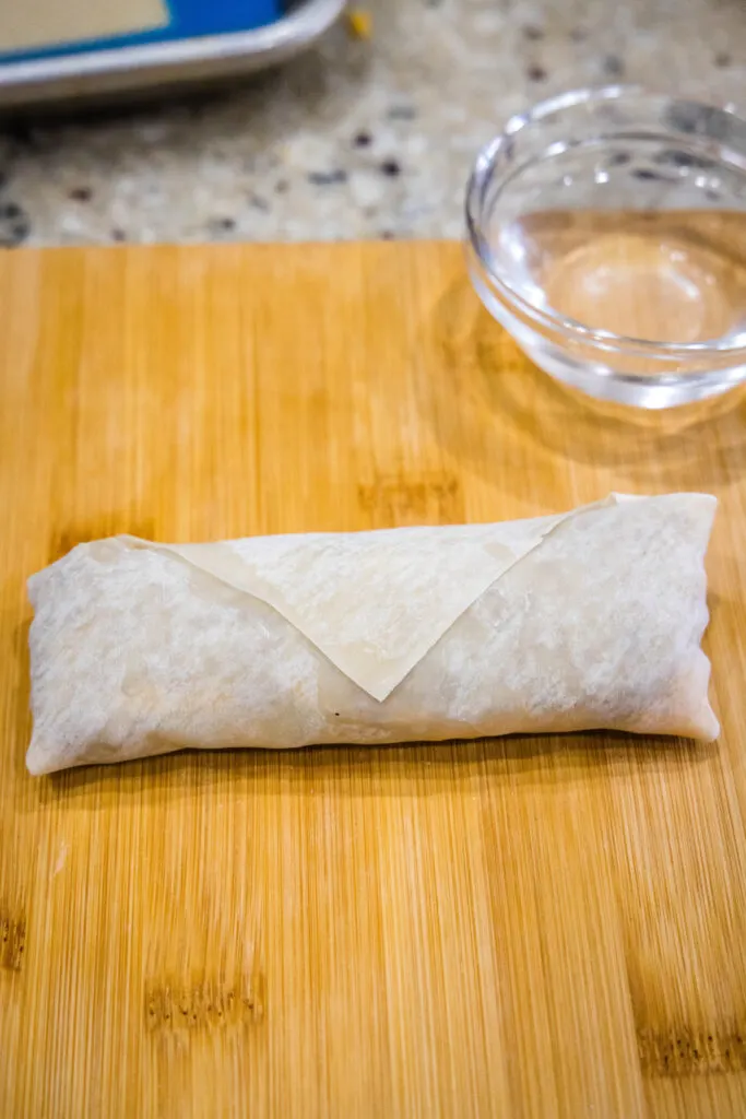 A rolled cheeseburger egg roll on a wooden surface.