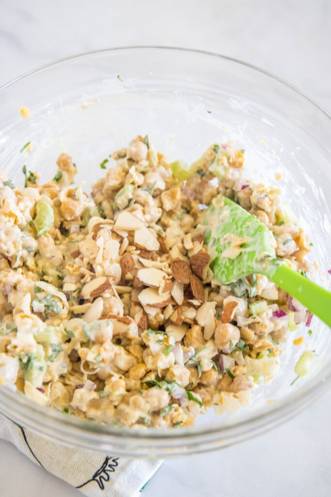 Chickpea chicken salad stirred together in a glass bowl with a green spoon.