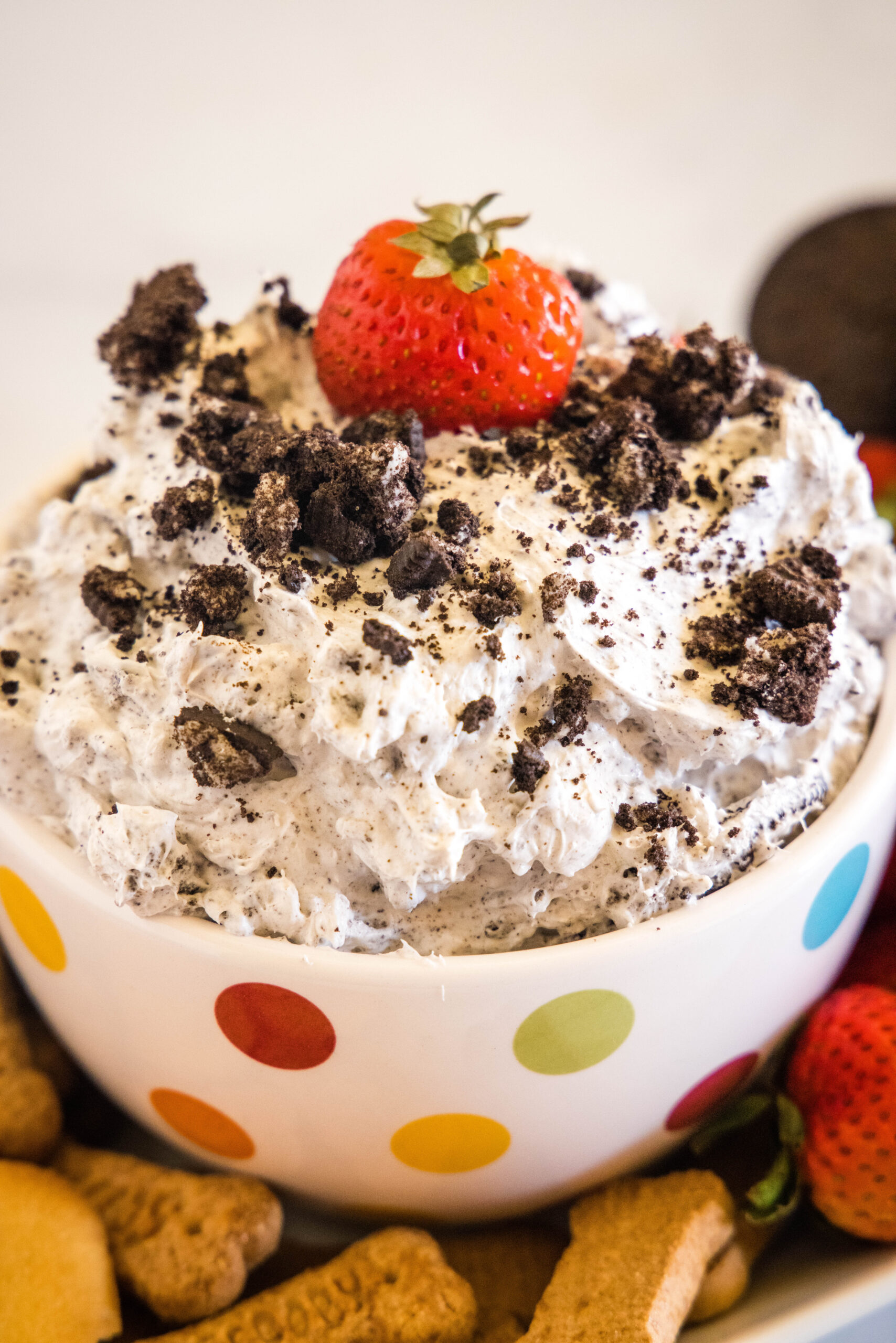 A bowl of Oreo fluff topped with crushed Oreos and a strawberry surrounded by a platter of dippables.