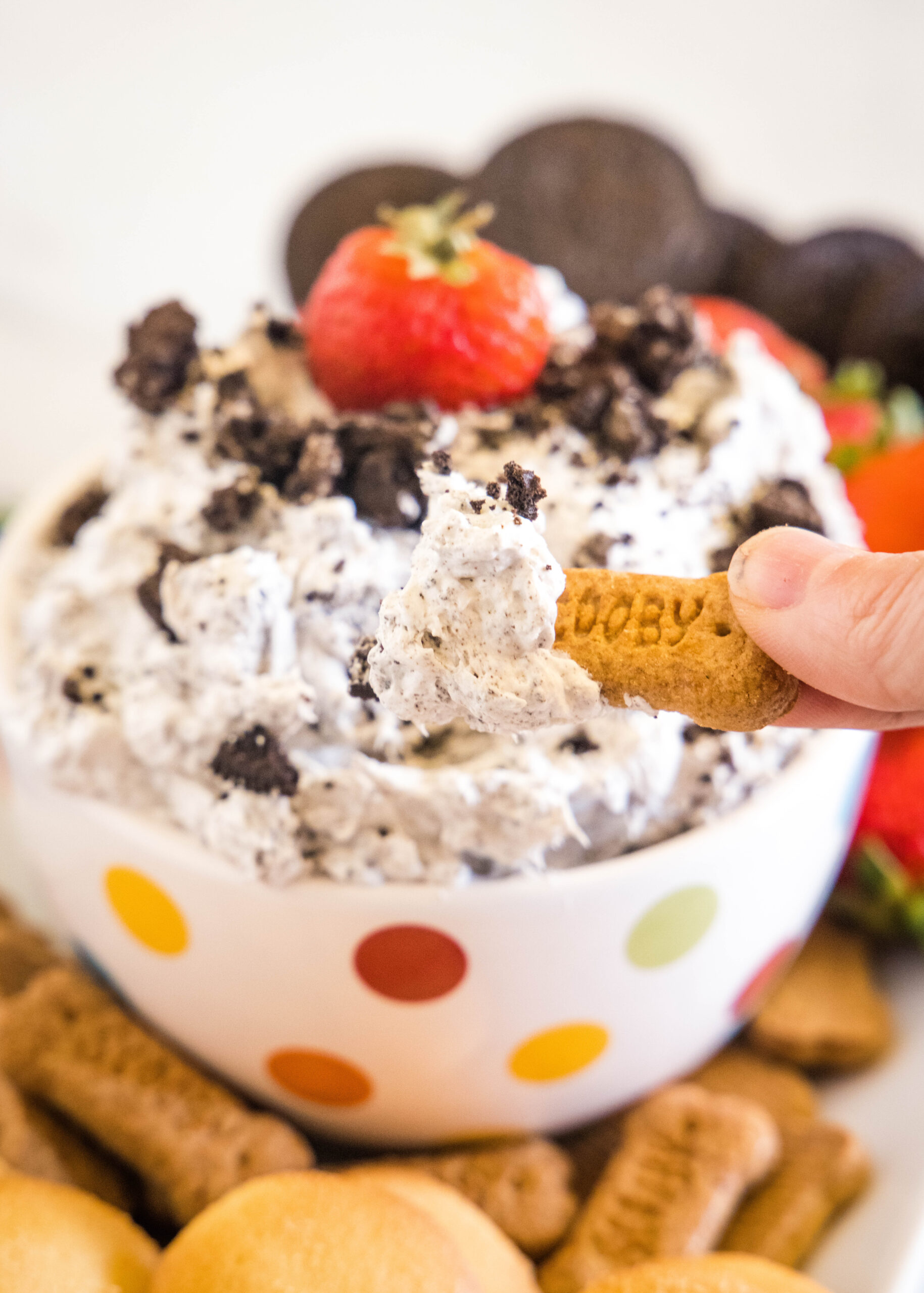 A hand dipping a cookie into a bowl of Oreo fluff.